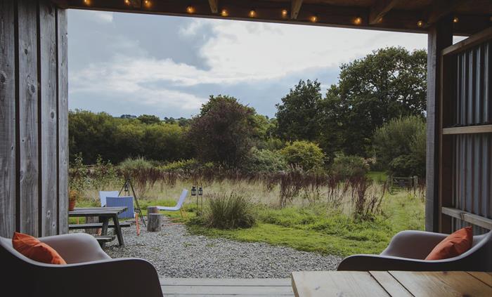 View from inside an open camp kitchen of a campfire scene and trees and hills in the background.